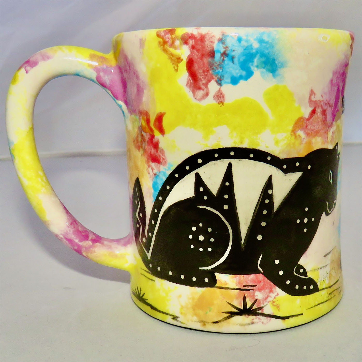 Image of Mana Pottery E-mug featuring cat on one side and desert vegetation on the other on a confetti background.