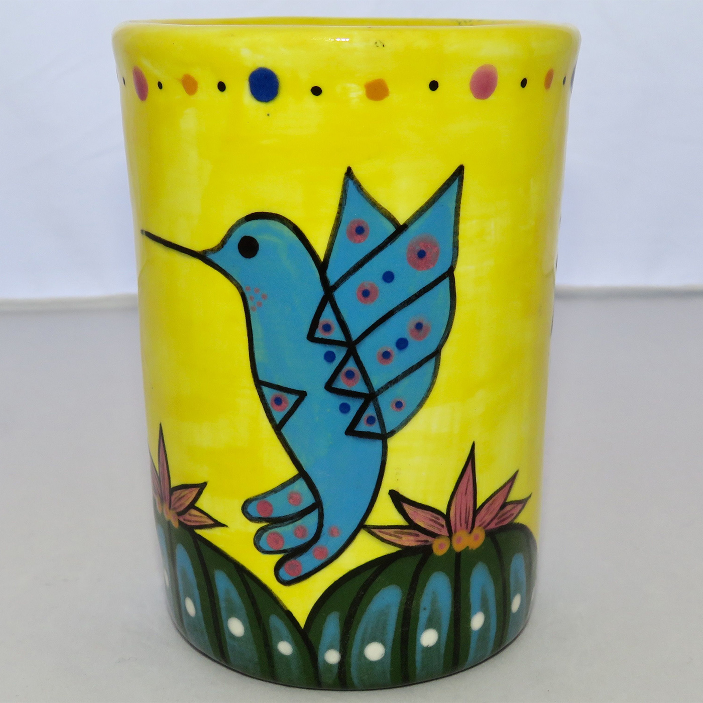 Mana Pottery Five Inch Tumbler featuring red and blue hummingbirds hovering over Peyote garden, on background of bright yellow.