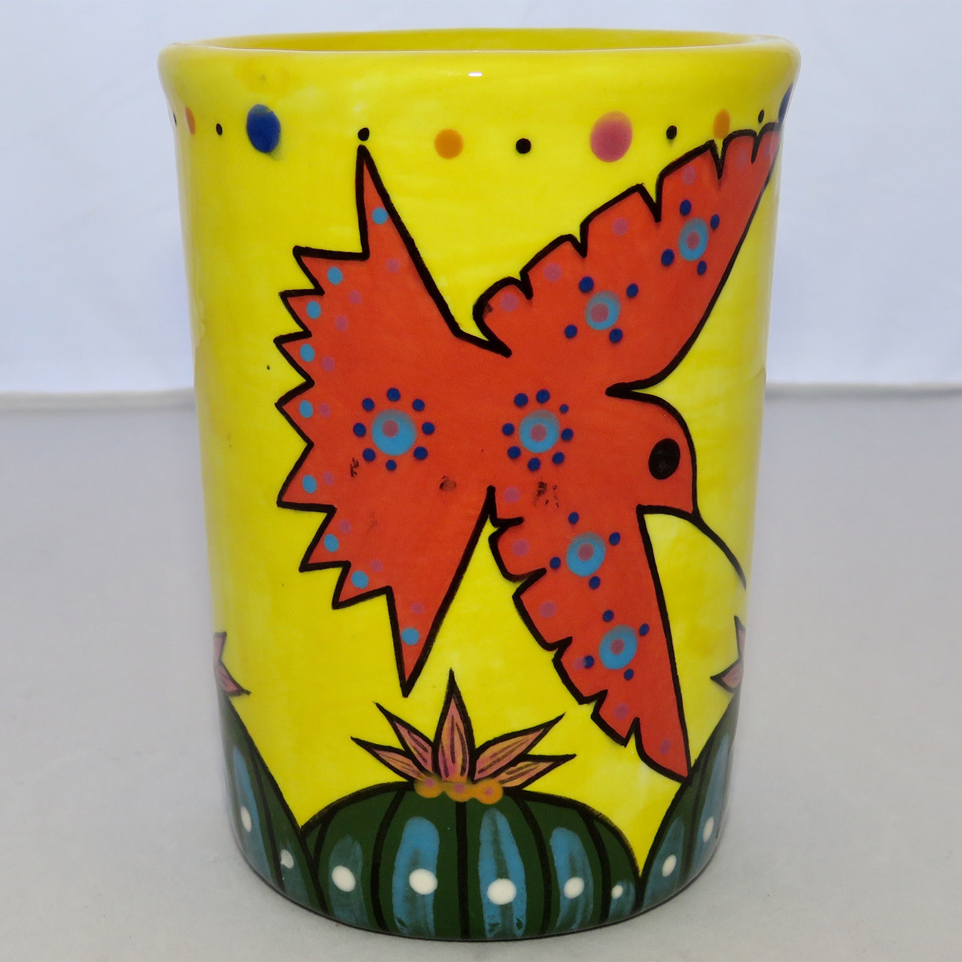 Mana Pottery Five Inch Tumbler featuring red and blue hummingbirds hovering over Peyote garden, on background of bright yellow.