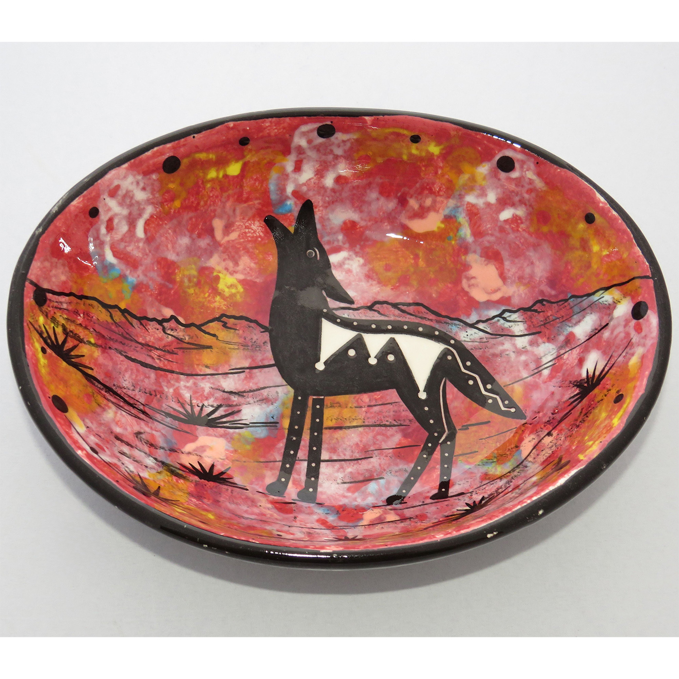 Photo of Mana Pottery Oval Bowl featuring howling coyote in desert on rose background, with black and white marbled underside.