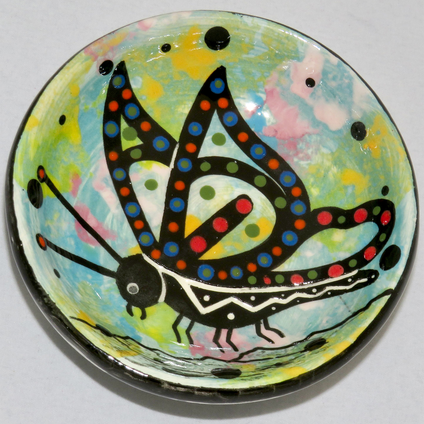 Image of Mana Pottery Holy Bowl featuring butterfly against turquoise blue and other colors. Underside view shows black and white marbled pattern.