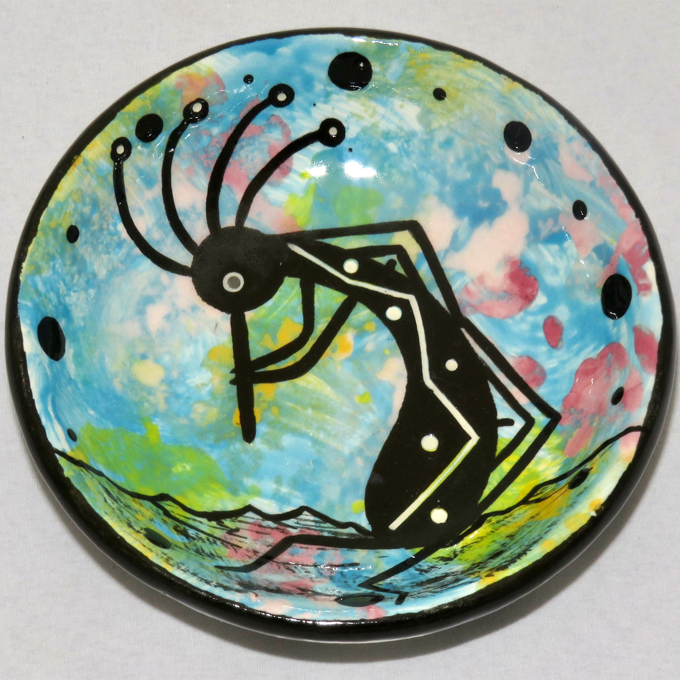 Image of Mana Pottery Holy Bowl featuring Kokopelli on turquoise blue and other colors. Underside view shows black and white marbled pattern.